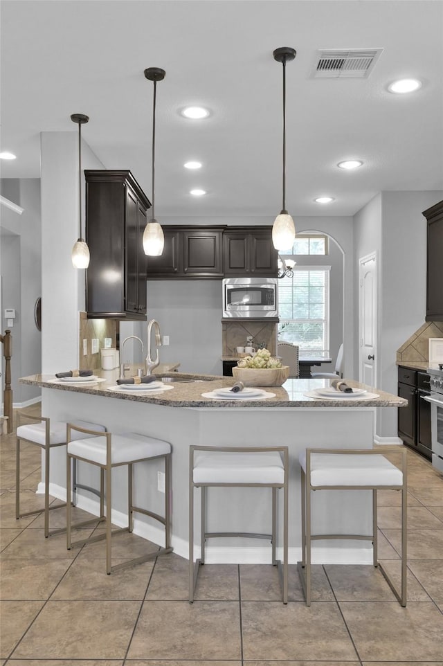 kitchen with a breakfast bar area, stainless steel appliances, a peninsula, visible vents, and backsplash