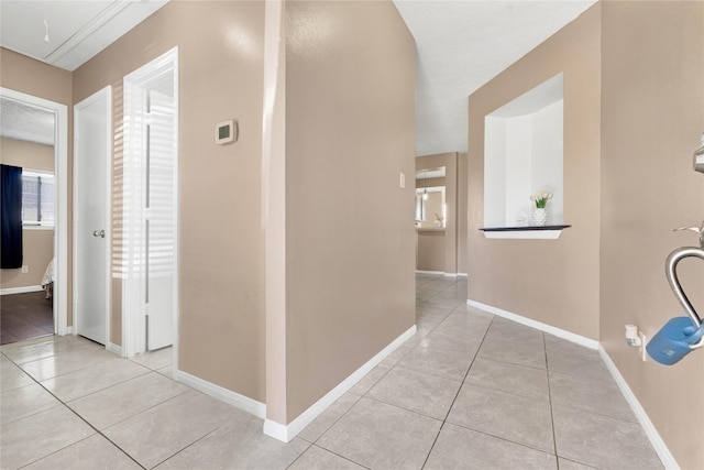 corridor with tile patterned flooring, attic access, and baseboards