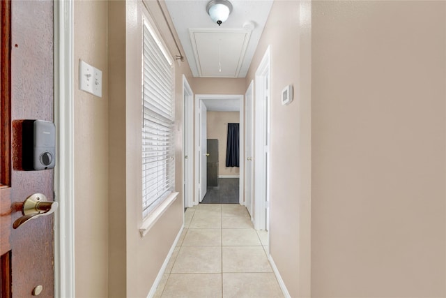 hall with attic access, light tile patterned flooring, and baseboards