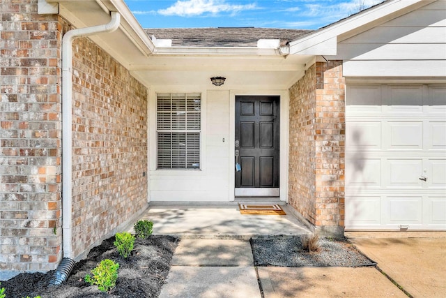 entrance to property with brick siding, roof with shingles, and an attached garage