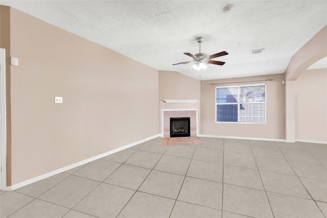 unfurnished living room with a textured ceiling, a tiled fireplace, a ceiling fan, and baseboards