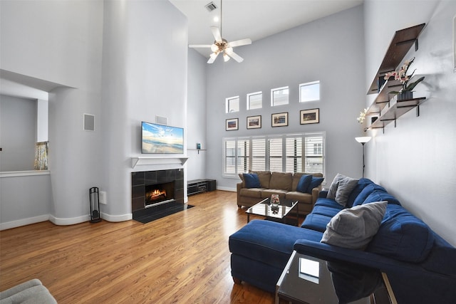 living area with a tiled fireplace, wood finished floors, visible vents, and baseboards