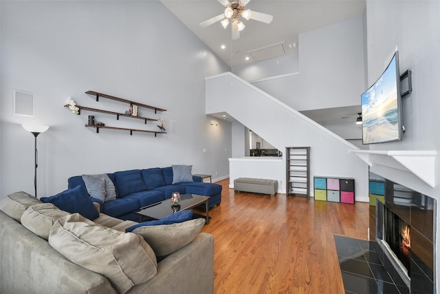 living area with a fireplace with flush hearth, wood finished floors, a towering ceiling, and ceiling fan