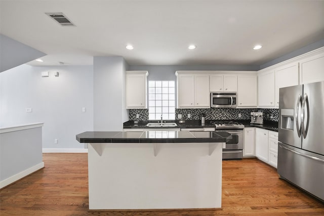 kitchen with visible vents, a kitchen breakfast bar, wood finished floors, white cabinets, and stainless steel appliances