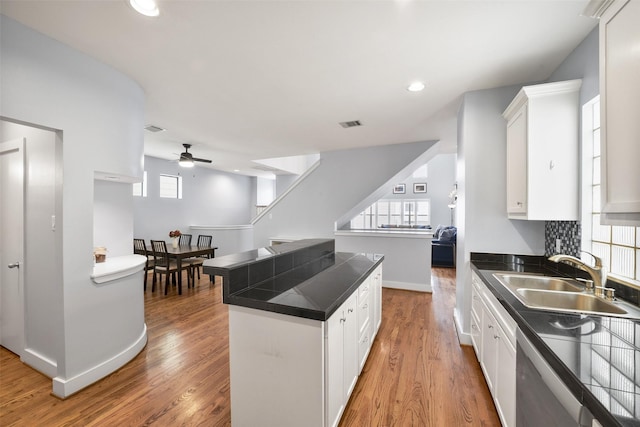 kitchen with white cabinetry, light wood-style flooring, a sink, dishwasher, and dark countertops