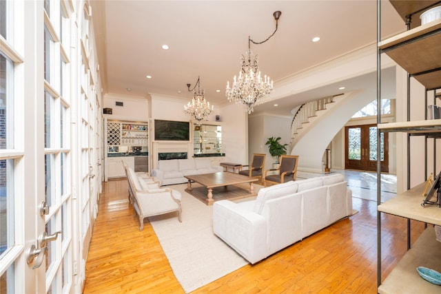 living area with french doors, a fireplace, an inviting chandelier, light wood-style floors, and stairs