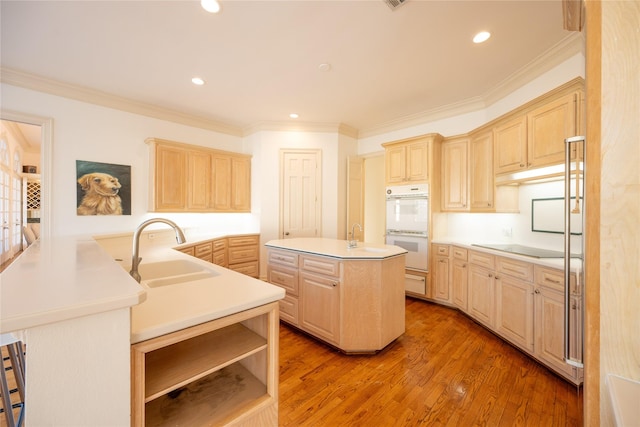 kitchen featuring ornamental molding, wood finished floors, a kitchen island with sink, double oven, and light brown cabinets