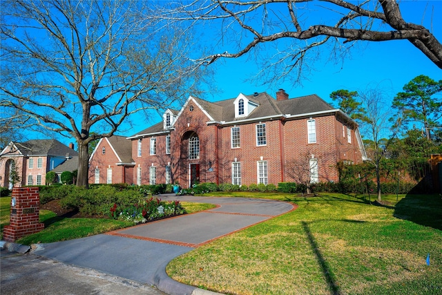 colonial home featuring brick siding, a chimney, and a front yard