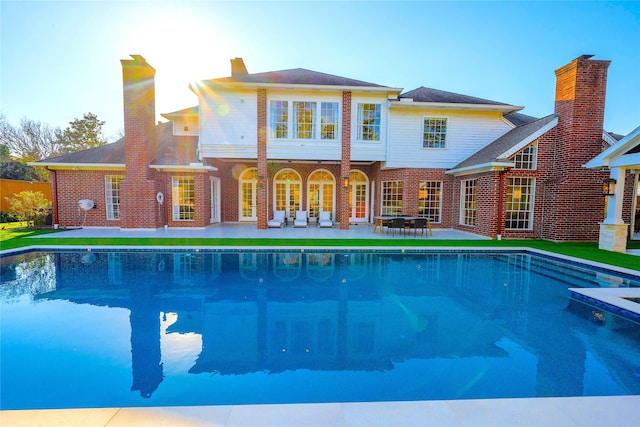 back of property featuring a patio area, a chimney, an outdoor pool, and brick siding