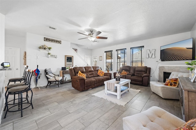 living area featuring visible vents, a textured ceiling, a ceiling fan, and a tile fireplace