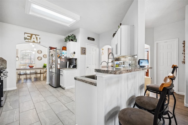 kitchen featuring a kitchen bar, a sink, stainless steel appliances, arched walkways, and a peninsula