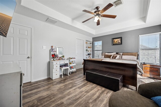 bedroom featuring a tray ceiling, wood finished floors, visible vents, and baseboards