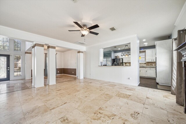 unfurnished living room featuring visible vents, baseboards, a ceiling fan, ornate columns, and crown molding