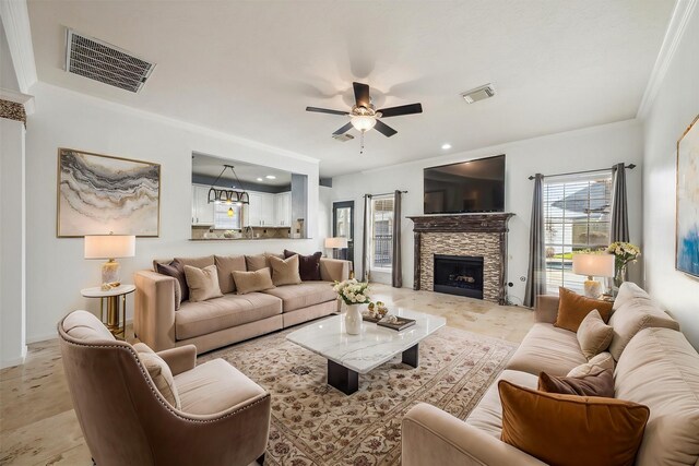 living room with ornamental molding, visible vents, ceiling fan, and a stone fireplace