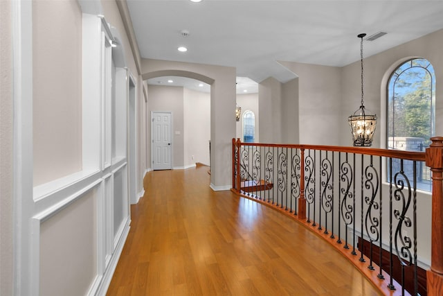 corridor featuring visible vents, baseboards, wood finished floors, arched walkways, and a notable chandelier