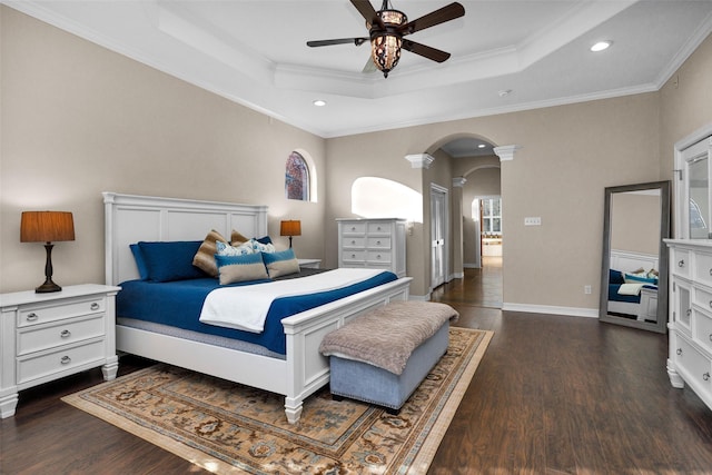 bedroom featuring a tray ceiling, crown molding, arched walkways, and dark wood-type flooring