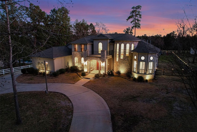 view of front of house featuring stone siding, a balcony, concrete driveway, and fence