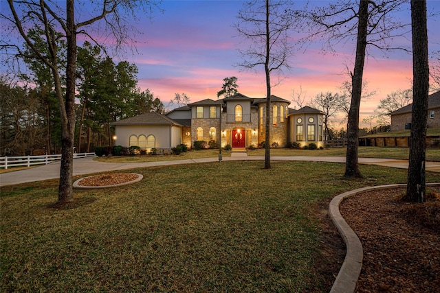 view of front of property with a yard, stone siding, stucco siding, and fence