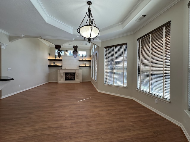 unfurnished living room featuring visible vents, a fireplace with raised hearth, wood finished floors, crown molding, and a raised ceiling