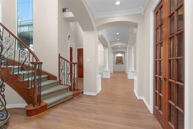 foyer with ornamental molding, arched walkways, light wood-style floors, baseboards, and ornate columns