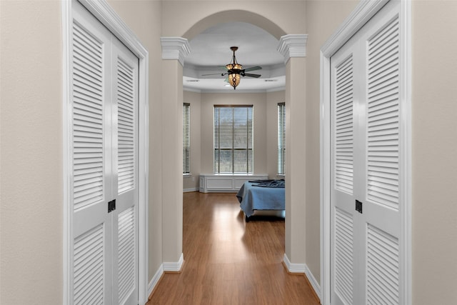 hall featuring crown molding, wood finished floors, arched walkways, and baseboards