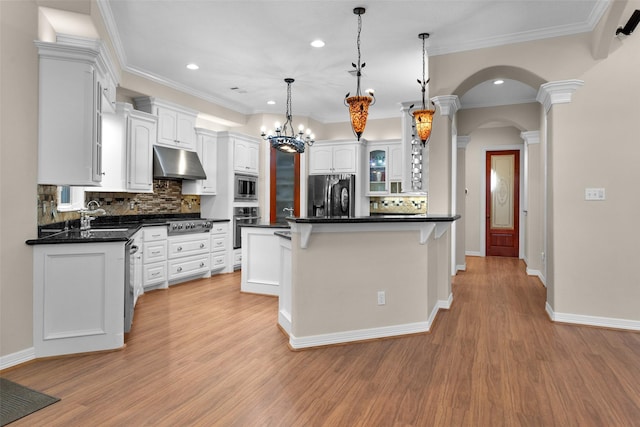 kitchen featuring under cabinet range hood, dark countertops, white cabinetry, arched walkways, and appliances with stainless steel finishes