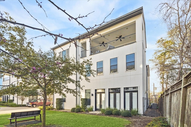 rear view of property featuring stucco siding, a lawn, central AC, fence, and a balcony