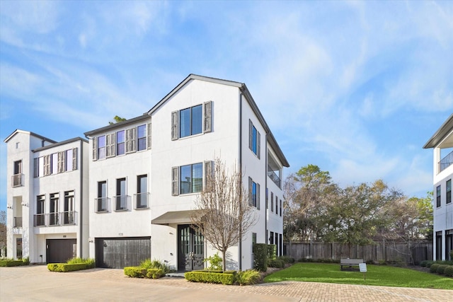 view of front facade featuring decorative driveway, stucco siding, fence, a garage, and a front lawn