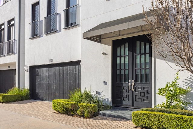 doorway to property featuring a garage, decorative driveway, and stucco siding