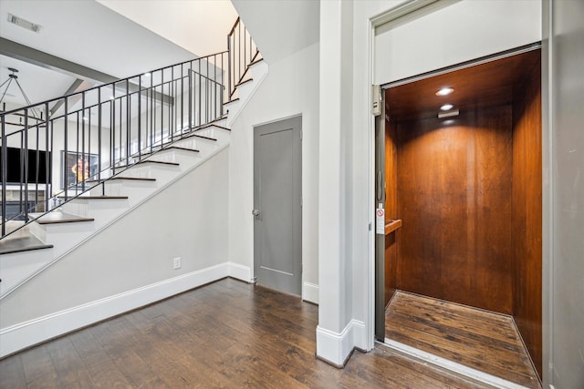 staircase with elevator, visible vents, baseboards, and wood finished floors