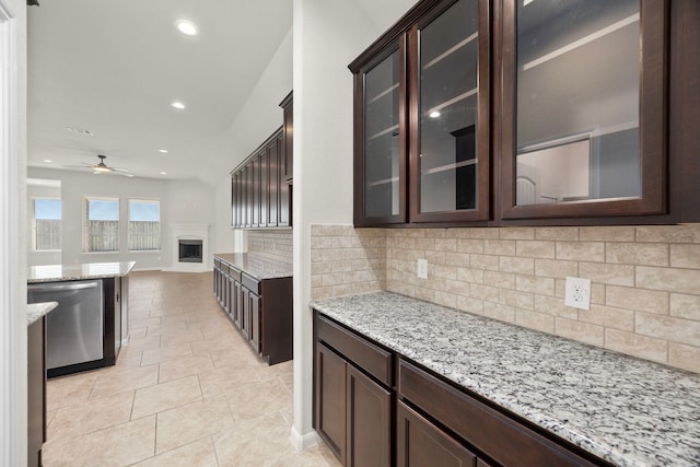 kitchen with light stone countertops, tasteful backsplash, dark brown cabinets, and dishwasher