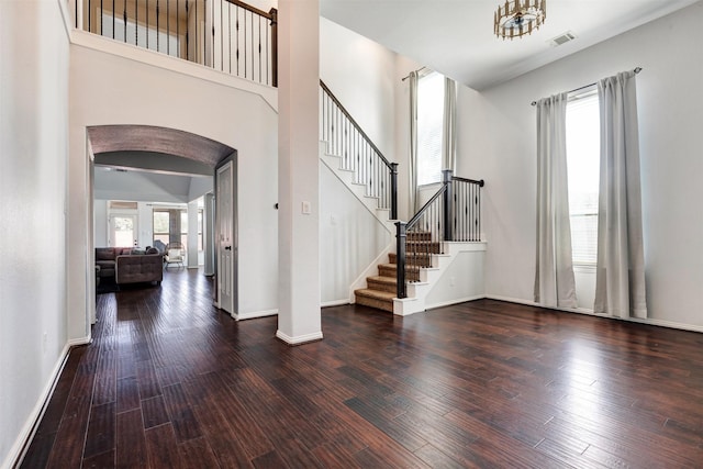 foyer entrance with arched walkways, visible vents, baseboards, and wood finished floors