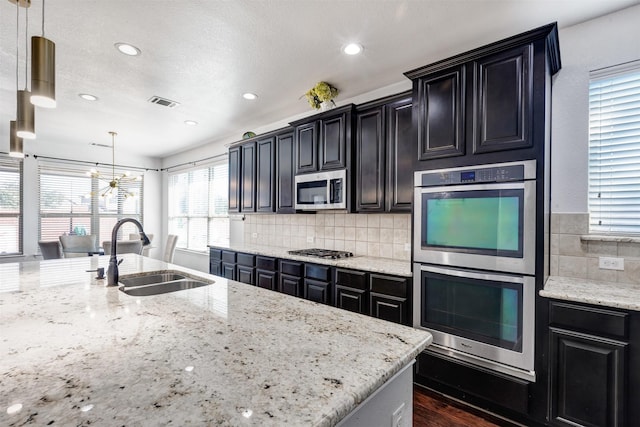 kitchen with visible vents, a sink, dark cabinetry, stainless steel appliances, and decorative backsplash