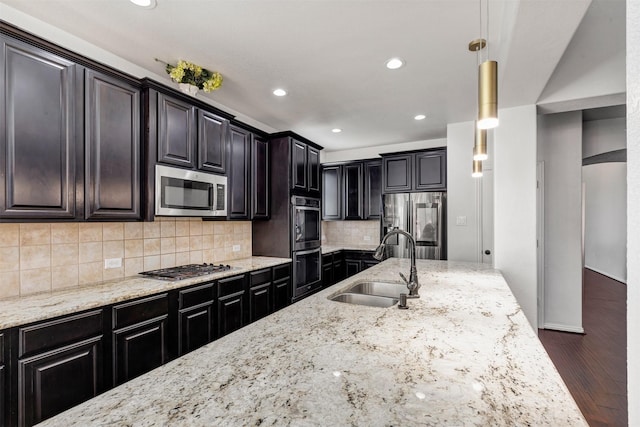 kitchen featuring light stone counters, dark wood finished floors, a sink, appliances with stainless steel finishes, and tasteful backsplash