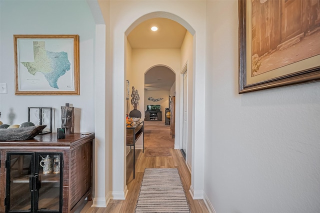 corridor featuring arched walkways, baseboards, and light wood finished floors