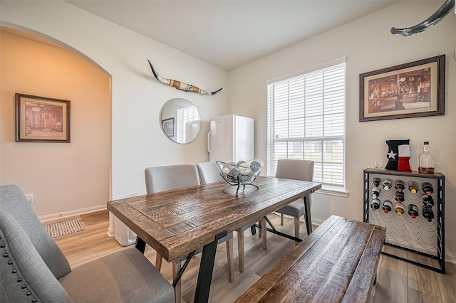 dining room featuring light wood-type flooring, baseboards, and arched walkways