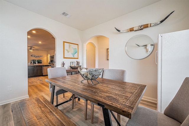 dining room with visible vents, arched walkways, baseboards, ceiling fan, and light wood-style flooring