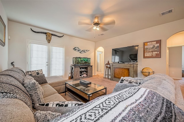 living room featuring carpet floors, arched walkways, visible vents, and ceiling fan