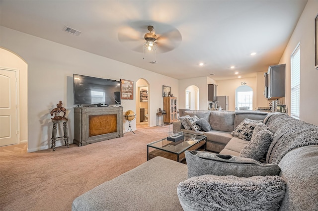 living area with arched walkways, recessed lighting, visible vents, light carpet, and ceiling fan