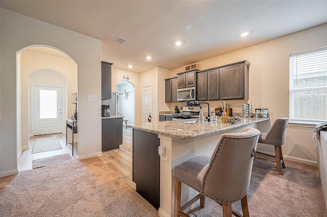 kitchen with appliances with stainless steel finishes, a peninsula, light stone countertops, a kitchen bar, and a sink