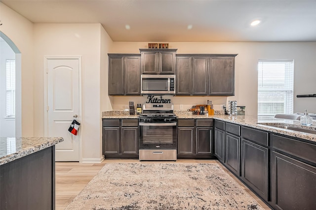 kitchen with arched walkways, light stone counters, light wood-style flooring, stainless steel appliances, and a sink