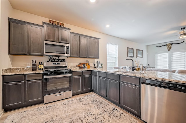 kitchen featuring light stone counters, appliances with stainless steel finishes, light wood-style floors, a sink, and dark brown cabinetry