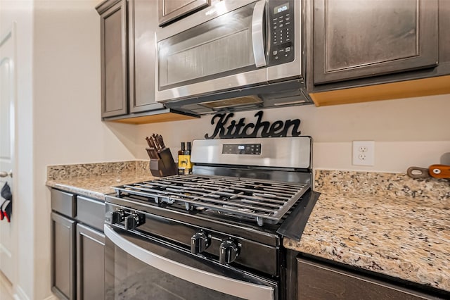 kitchen with dark brown cabinetry, appliances with stainless steel finishes, and light stone counters