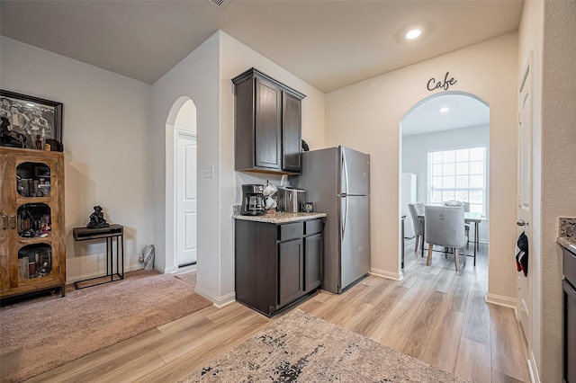 kitchen with light wood-style floors, freestanding refrigerator, arched walkways, and light stone countertops