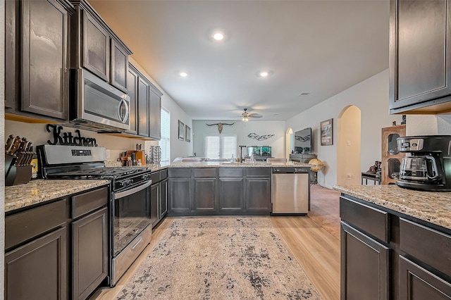 kitchen featuring arched walkways, open floor plan, appliances with stainless steel finishes, light stone countertops, and light wood finished floors