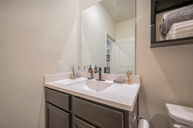 bathroom with a textured wall, vanity, and toilet