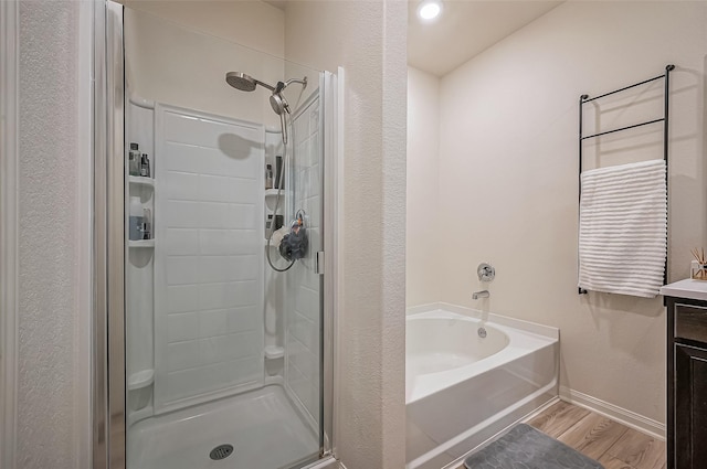 bathroom featuring baseboards, wood finished floors, vanity, a shower stall, and a bath