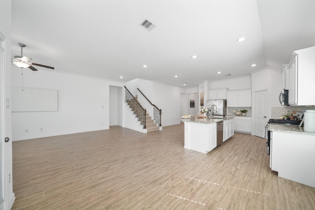 kitchen with a center island with sink, visible vents, decorative backsplash, appliances with stainless steel finishes, and open floor plan