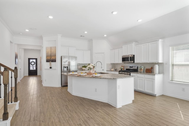 kitchen with a kitchen island with sink, stainless steel appliances, a sink, light wood-type flooring, and tasteful backsplash