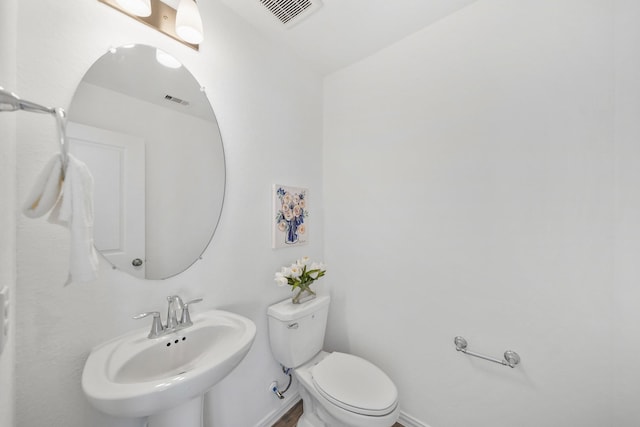 half bathroom featuring toilet, baseboards, visible vents, and a sink